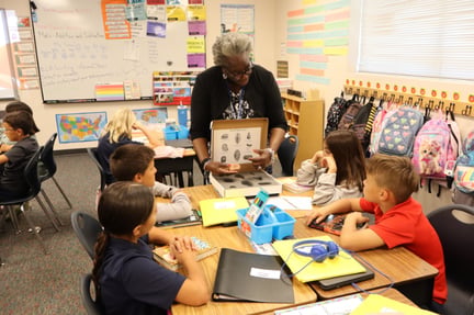 Young students sitting at their tables looking at the teacher showing them fossils