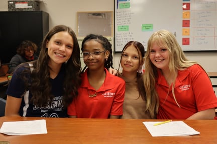 pre teen students sitting at a classroom desk smiling